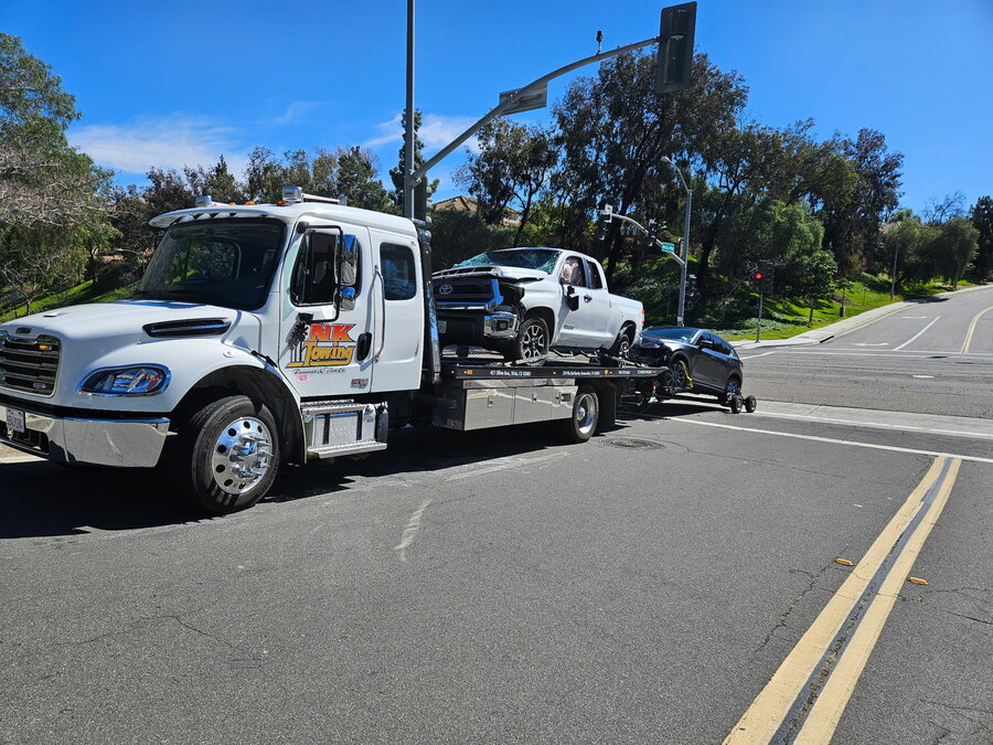 NK Towing flatbed hauling an accident-damaged truck and SUV