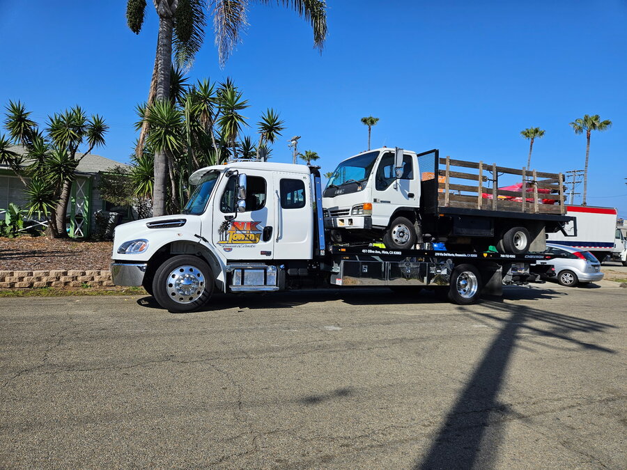 NK Towing flatbed hauling a utility truck